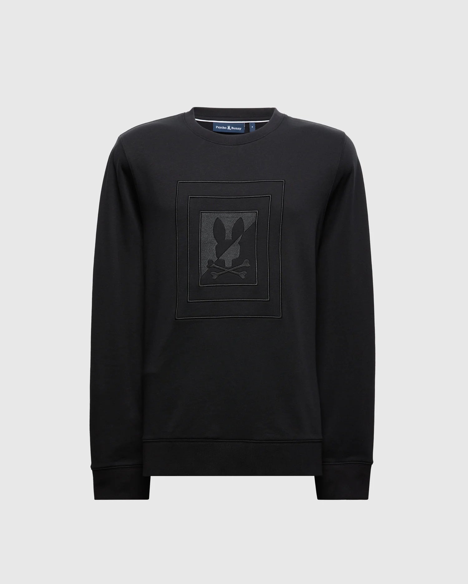 The MENS OAK CITY CREW NECK - B6S274E200 by Psycho Bunny is a premium black sweatshirt with a lightweight crew neck and long sleeves. It features subtle raised embroidery of a stylized rabbit and crossbones design on the chest, set against a plain light gray background.