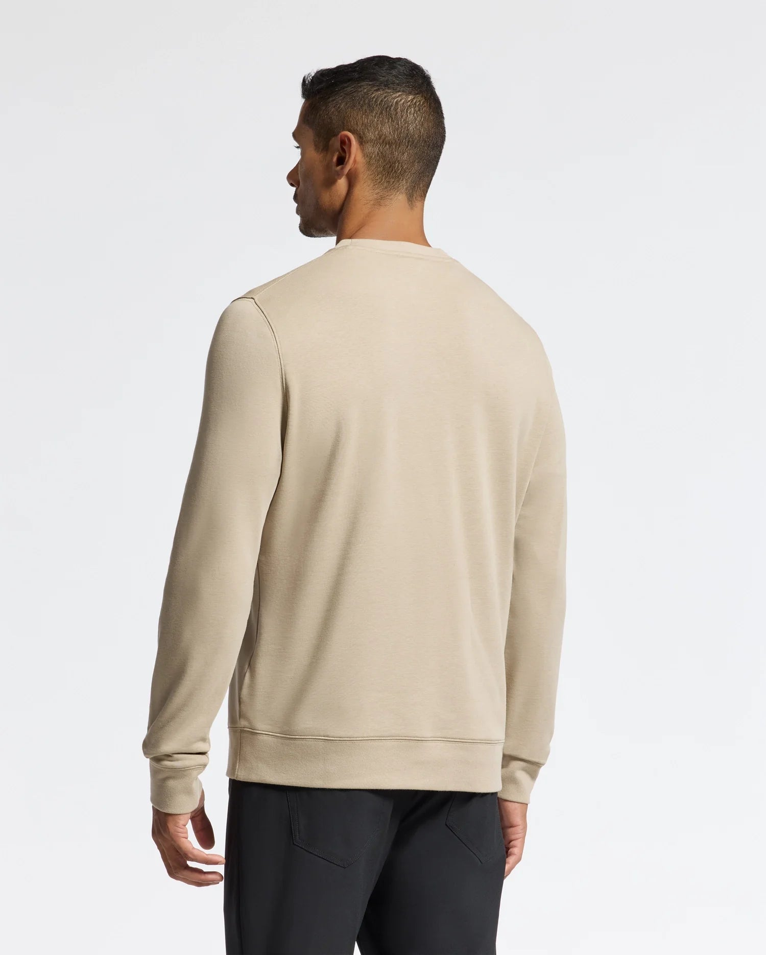 A person wearing a Psycho Bunny Men's Oak City Crew Neck - B6S274E200 sweater and black pants is standing with their back to the camera. The background is a plain white wall, accentuating the elegance of their outfit.