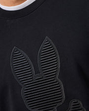 Close-up of a black cotton jersey shirt featuring embossed, vertical line patterns that create bunny ears and a face. The shirt's texture is accentuated by the lighting, with a glimpse of a white neckline at the top, reminiscent of the style seen in the MENS KINGSTON SWEATSHIRT - B6S480D200 by Psycho Bunny.