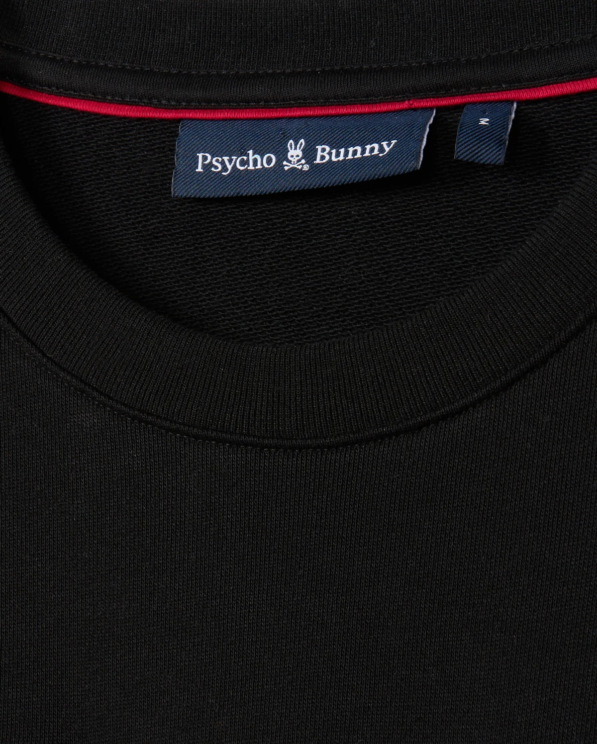 Close-up of the MENS KINGSTON SWEATSHIRT - B6S480D200 by Psycho Bunny, crafted from lush black cotton jersey. It features a label near the neckline with "Psycho Bunny" and the iconic bunny embroidery logo. A distinct red line adds contrast inside the collar.