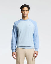 A person in a Psycho Bunny MENS ARCHIE SWEATSHIRT, B6S630F200, mixes light blue and navy tones with beige cargo pants, standing against a white backdrop for a monochrome look.