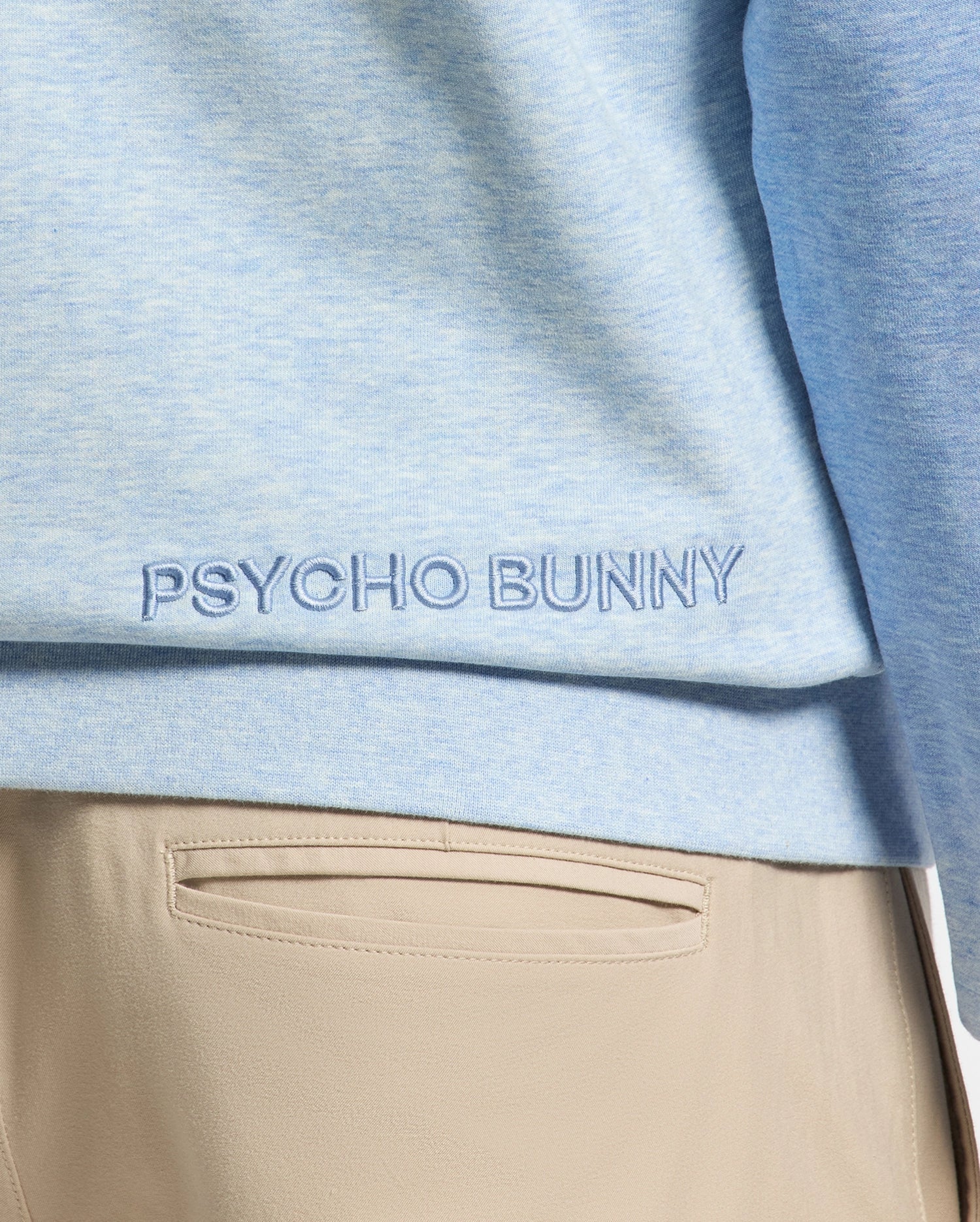 Close-up of a person in a light blue cotton MENS ARCHIE SWEATSHIRT - B6S630F200 by Psycho Bunny, with matching embroidery. They wear light tan pants, highlighting effortless monochrome styling.