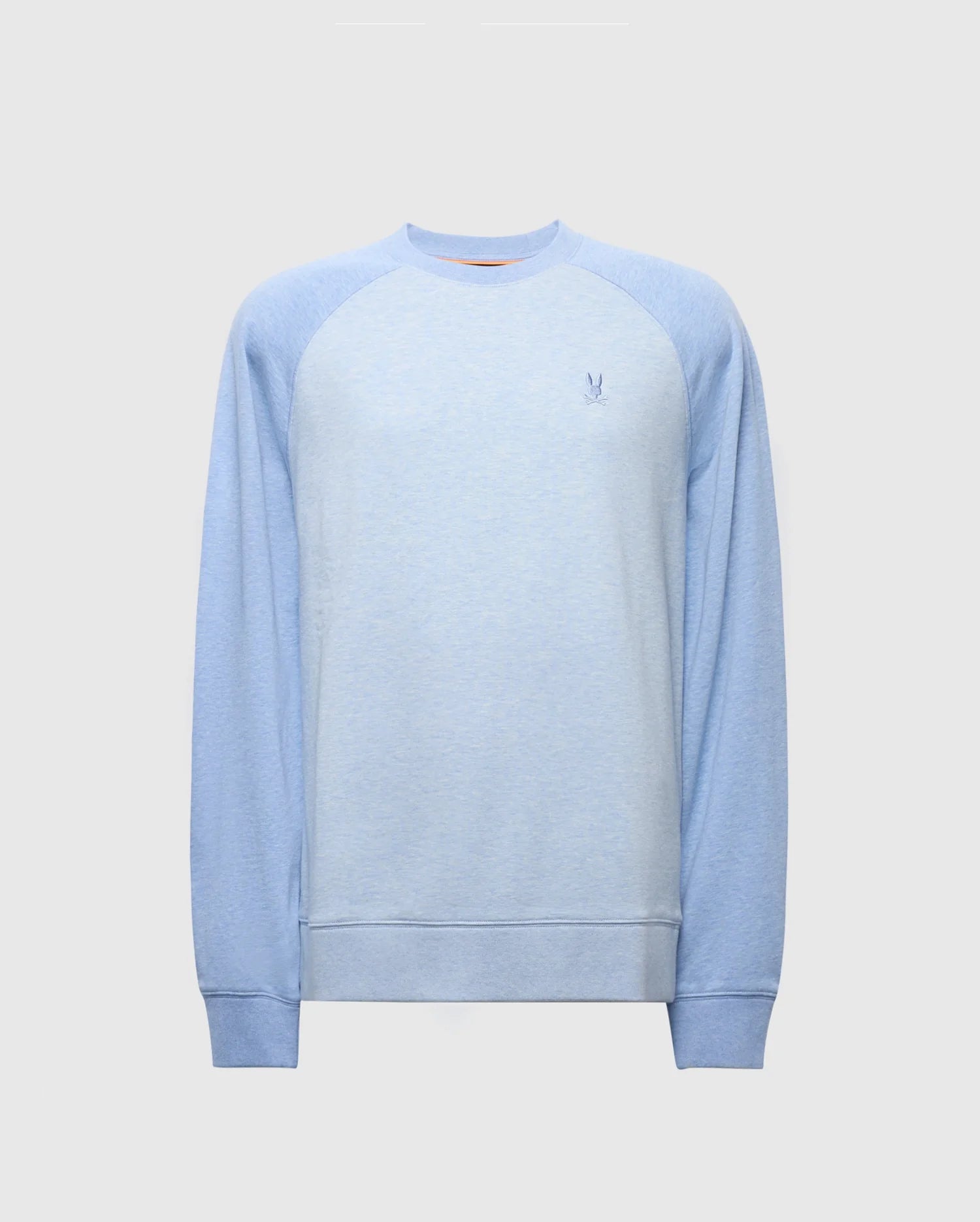 The Psycho Bunny MENS ARCHIE SWEATSHIRT - B6S630F200 is a light blue cotton jersey with faded raglan sleeves and a small embroidered Bunny logo on the chest. It features ribbed cuffs and hem, perfect for monochrome styling against a plain light gray background.