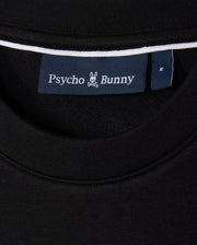 A close-up of the black Men's Courtside Sweatshirt's neckline showcasing a blue label with a white bunny logo and "Psycho Bunny" branding. Made from a breathable cotton-blend, this piece fuses courtside sweatshirt style with tennis-inspired flair.