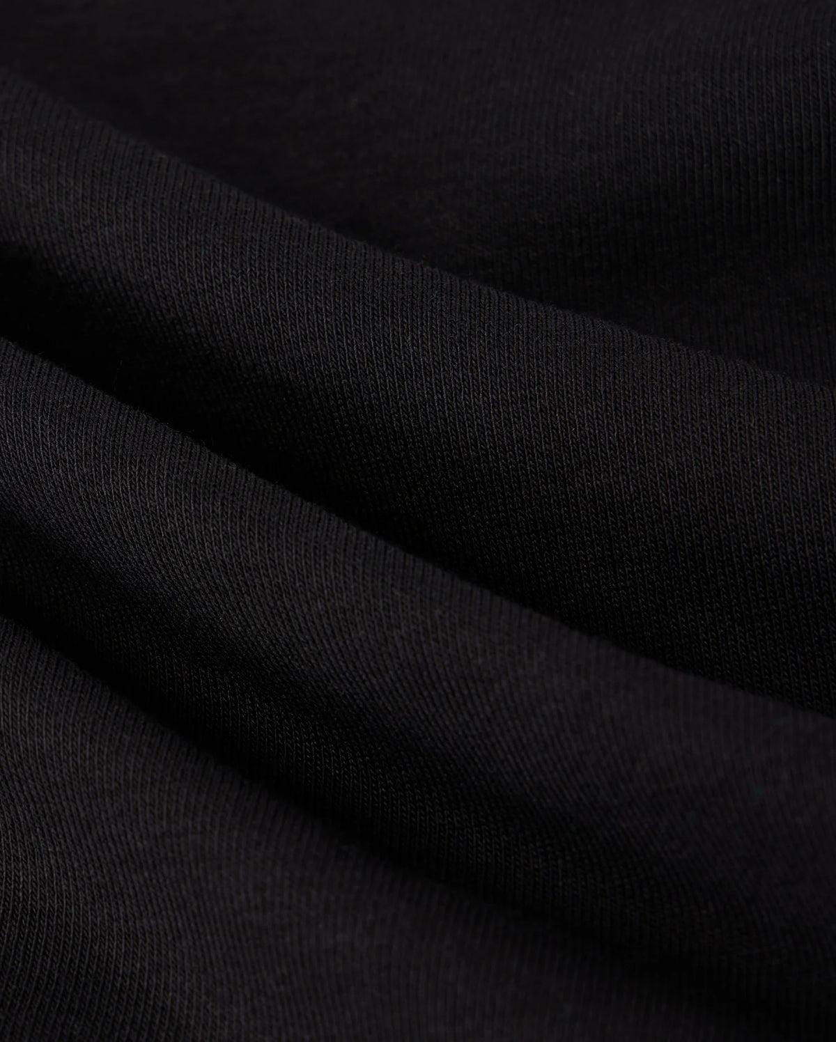 A close-up image reveals the black fabric of the MENS COURTSIDE SWEATSHIRT - B6S688C200 by Psycho Bunny, showcasing a soft, slightly wavy texture with a visible weave pattern. The smooth and stretchy material features subtle shadows that enhance its folds, offering a tennis-inspired elegance reminiscent of its design.