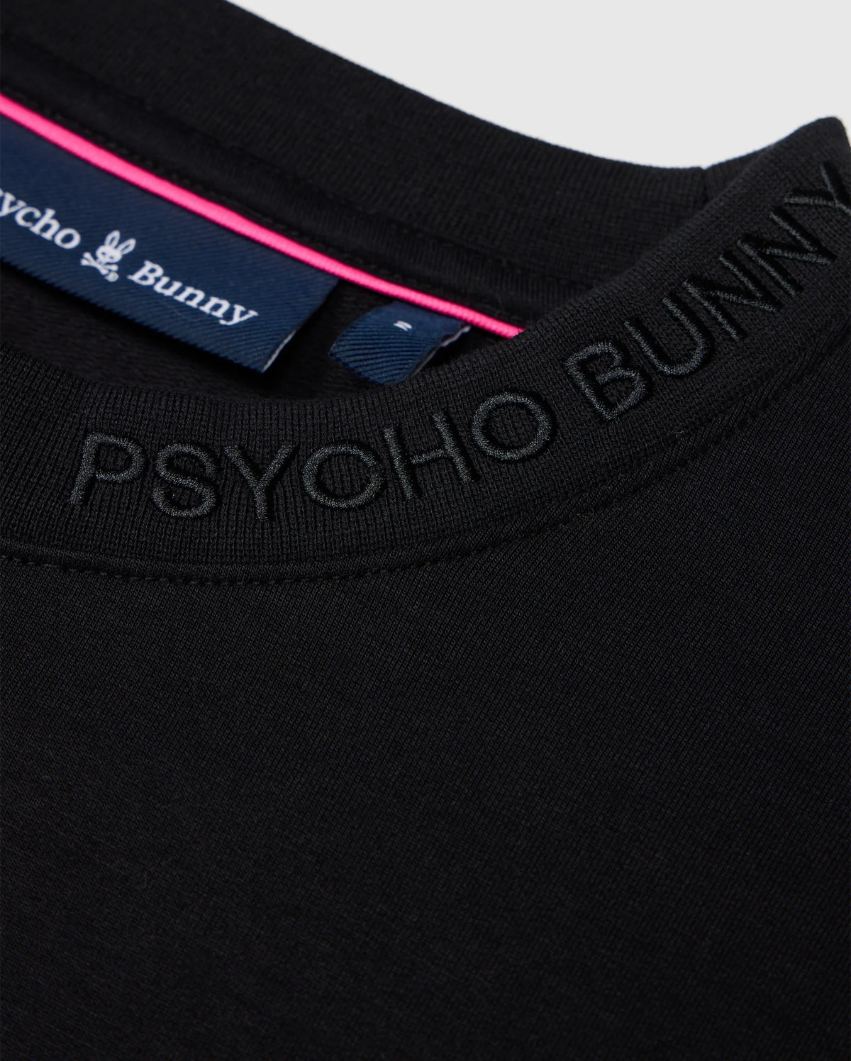 Close-up of a black Psycho Bunny Men's Duke Embroidered Sweatshirt, made from a soft cotton-blend, featuring the logo around the neckline. The visible collar tag displays the brand name with a pink stripe, enhancing its luxurious pullover appeal.