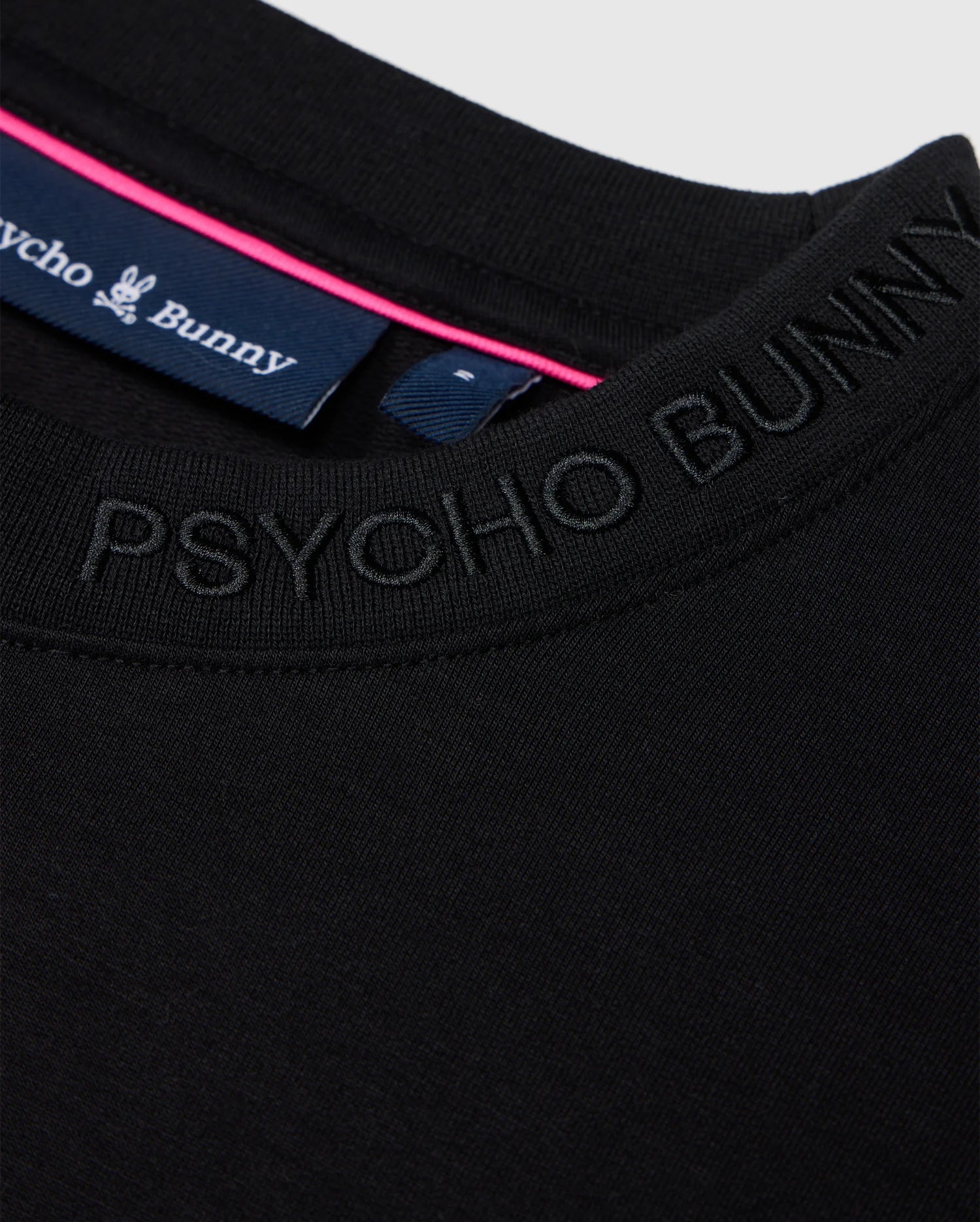 Close-up of a black Psycho Bunny Men's Duke Embroidered Sweatshirt, made from a soft cotton-blend, featuring the logo around the neckline. The visible collar tag displays the brand name with a pink stripe, enhancing its luxurious pullover appeal.