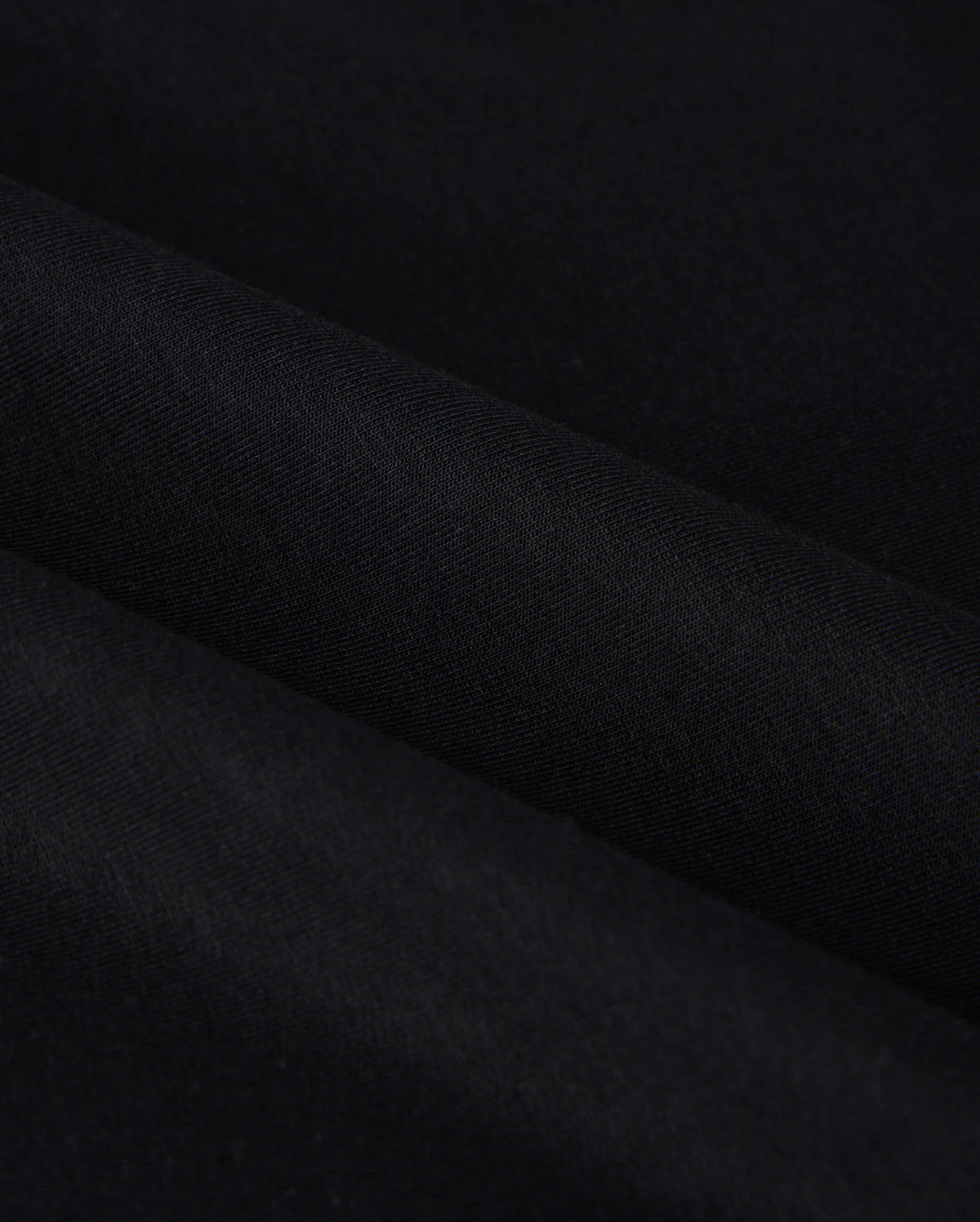 Close-up of the MENS DUKE EMBROIDERED SWEATSHIRT - B6S706D200 from Psycho Bunny, featuring a black cotton-blend fabric with a smooth texture and subtle diagonal folds. The image emphasizes the sweatshirt's dark, uniform color and soft, even surface reminiscent of luxury apparel.