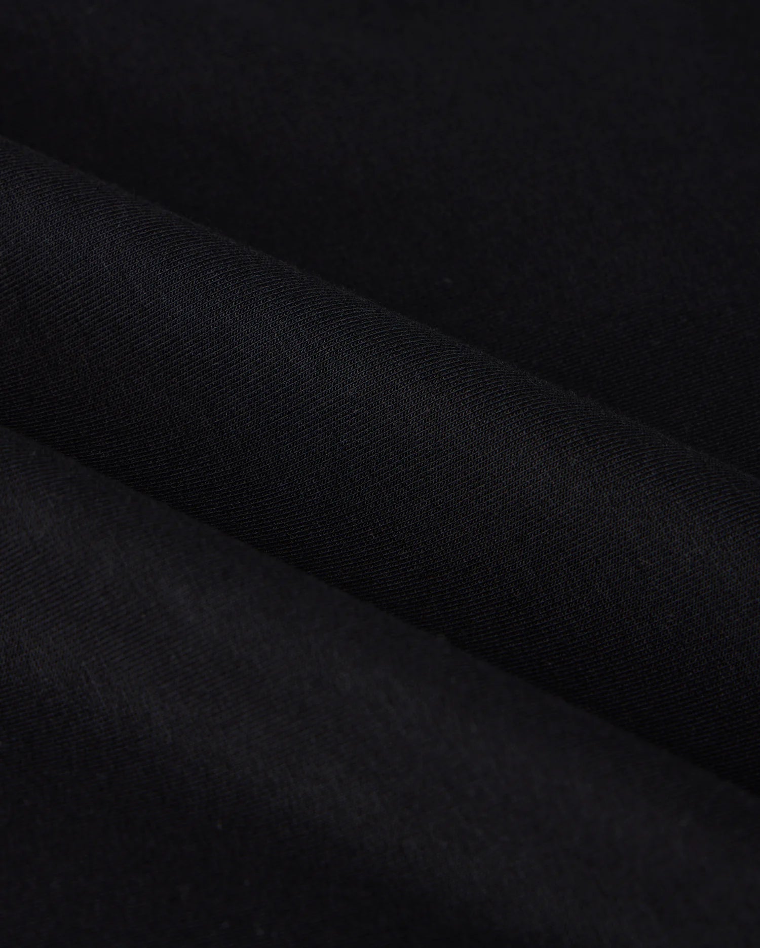 Close-up of the MENS DUKE EMBROIDERED SWEATSHIRT - B6S706D200 from Psycho Bunny, featuring a black cotton-blend fabric with a smooth texture and subtle diagonal folds. The image emphasizes the sweatshirt's dark, uniform color and soft, even surface reminiscent of luxury apparel.