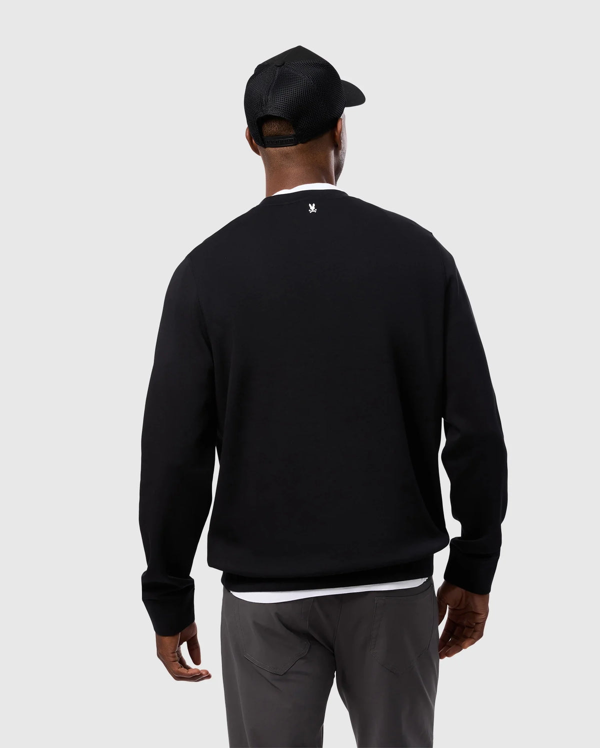 A person wearing the Psycho Bunny MENS TACOMA MODAL SWEATSHIRT - B6S927D200 in black, crafted from premium modal fabric, pairs it with gray pants and a black cap, standing with their back to the camera. The sweatshirt showcases a small white logo at the neck, providing both style and luxurious comfort against a light gray background.
