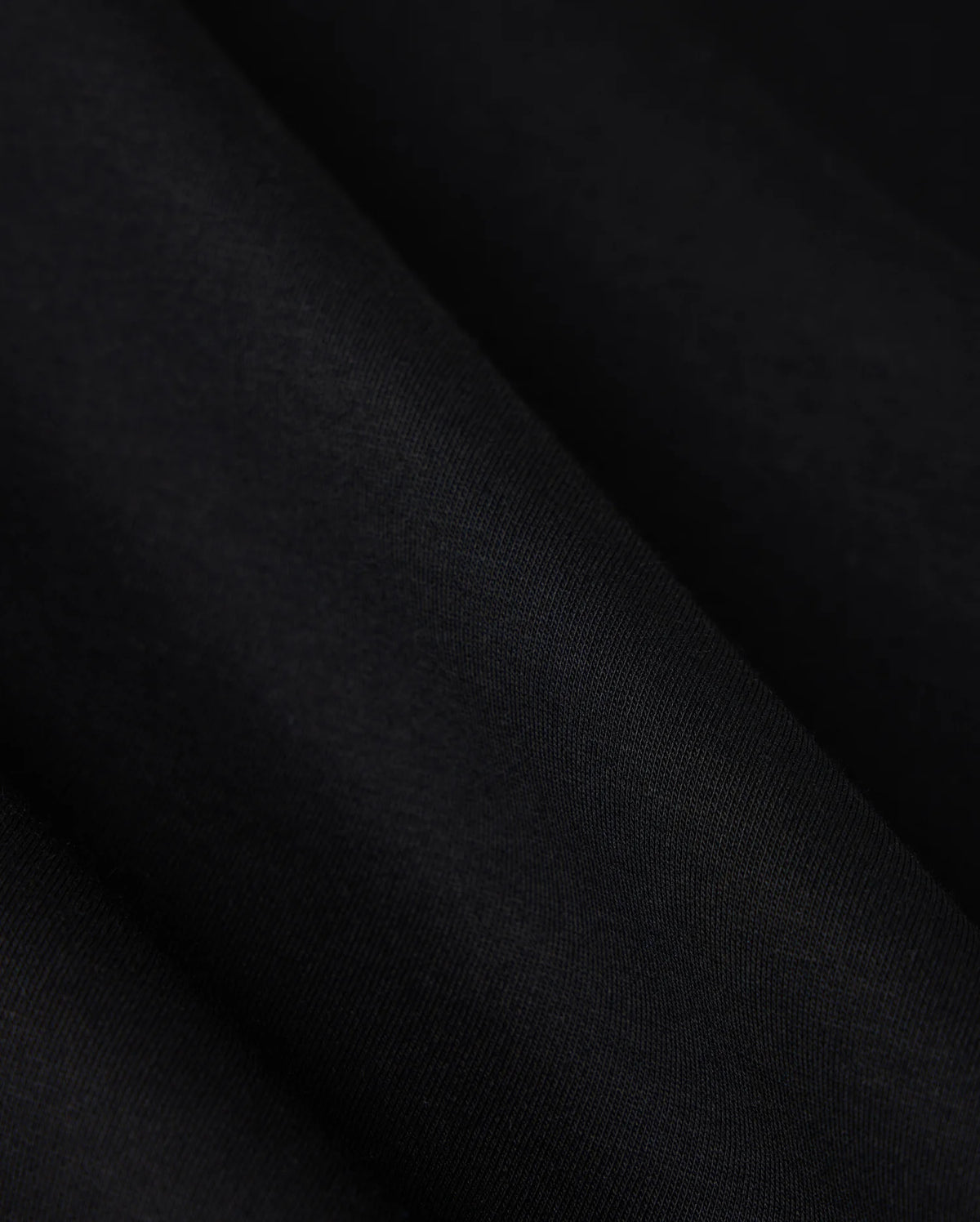 A close-up image showcasing the luxurious comfort of the Psycho Bunny MENS TACOMA MODAL SWEATSHIRT - B6S927D200, featuring a smooth, dark black premium modal fabric with subtle texture and folds that create gentle shadows on its surface.