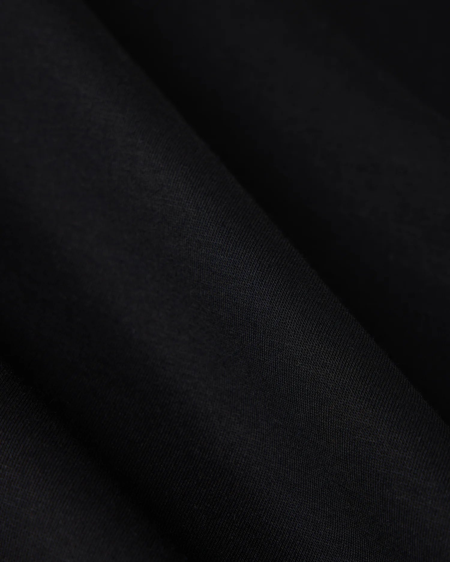 A close-up image showcasing the luxurious comfort of the Psycho Bunny MENS TACOMA MODAL SWEATSHIRT - B6S927D200, featuring a smooth, dark black premium modal fabric with subtle texture and folds that create gentle shadows on its surface.