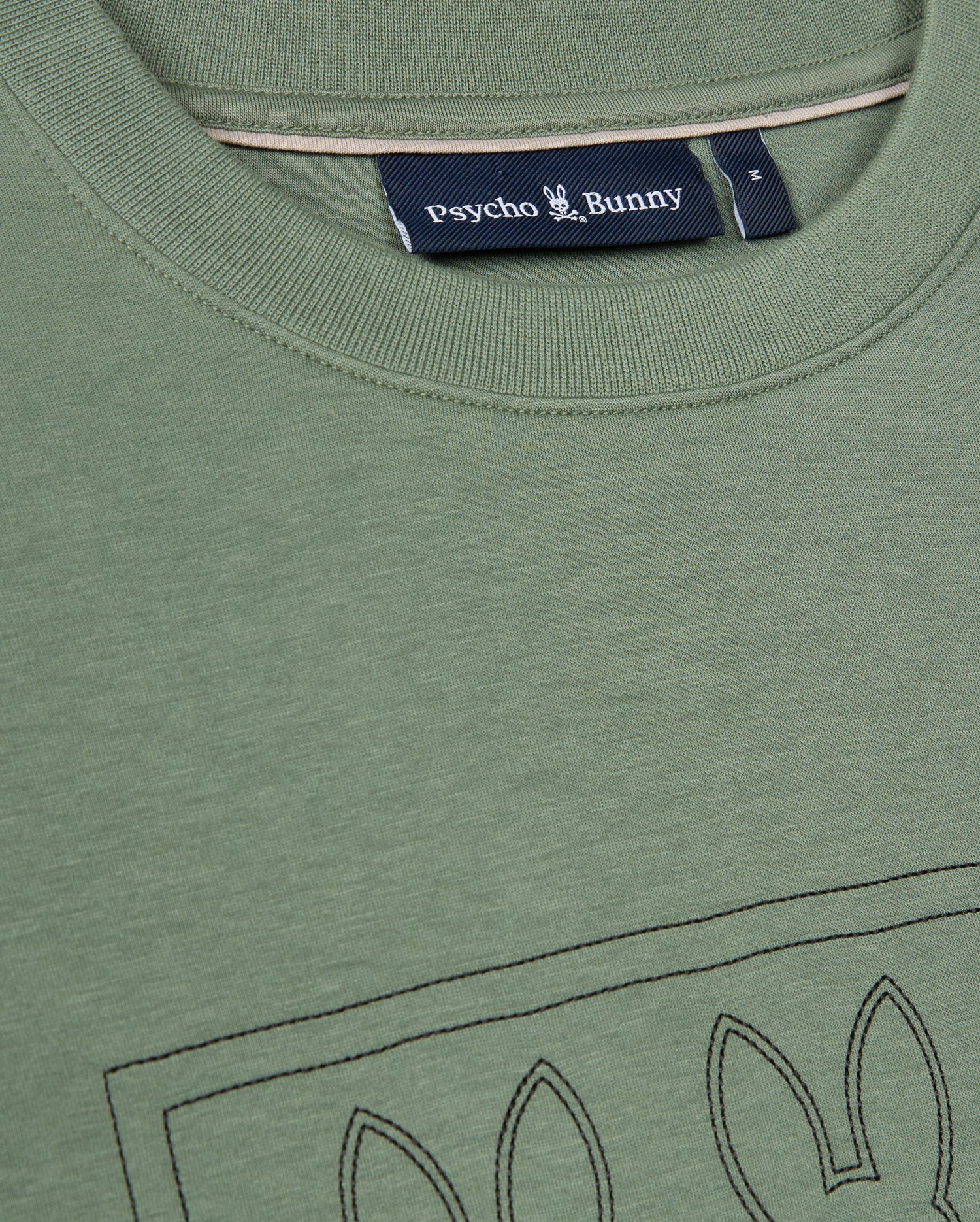 A close-up view of the green Mens Tacoma Sweatshirt by Psycho Bunny highlights its luxurious comfort and stitched bunny ear outline on the front, with the label prominently displayed beneath the collar. The premium stretch fabric guarantees a perfect fit while maintaining a lightweight feel.