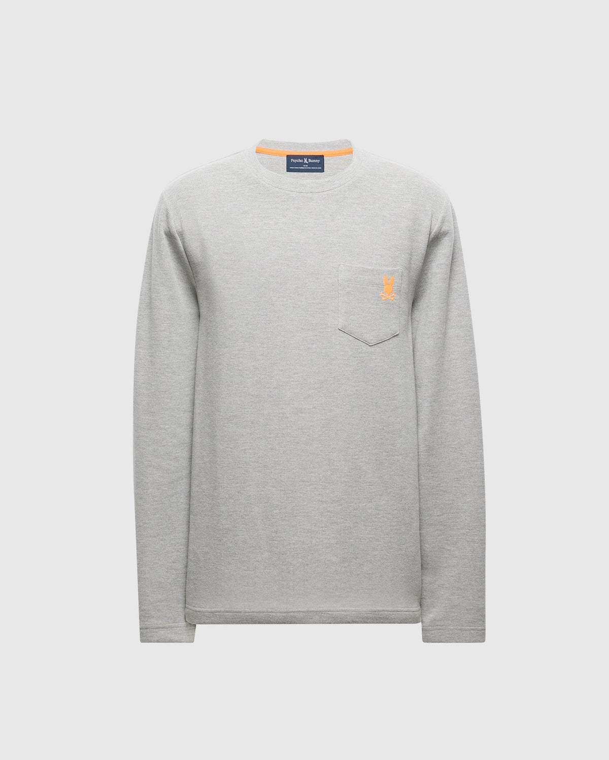 The Psycho Bunny MENS VAIL WAFFLE LOUNGE LONG SLEEVE TEE - B6T672E200 is a stylish men's light gray waffle knit tee with a crew neckline and a chest pocket on the left side. It features a small orange embroidered logo and is displayed on a plain white background.