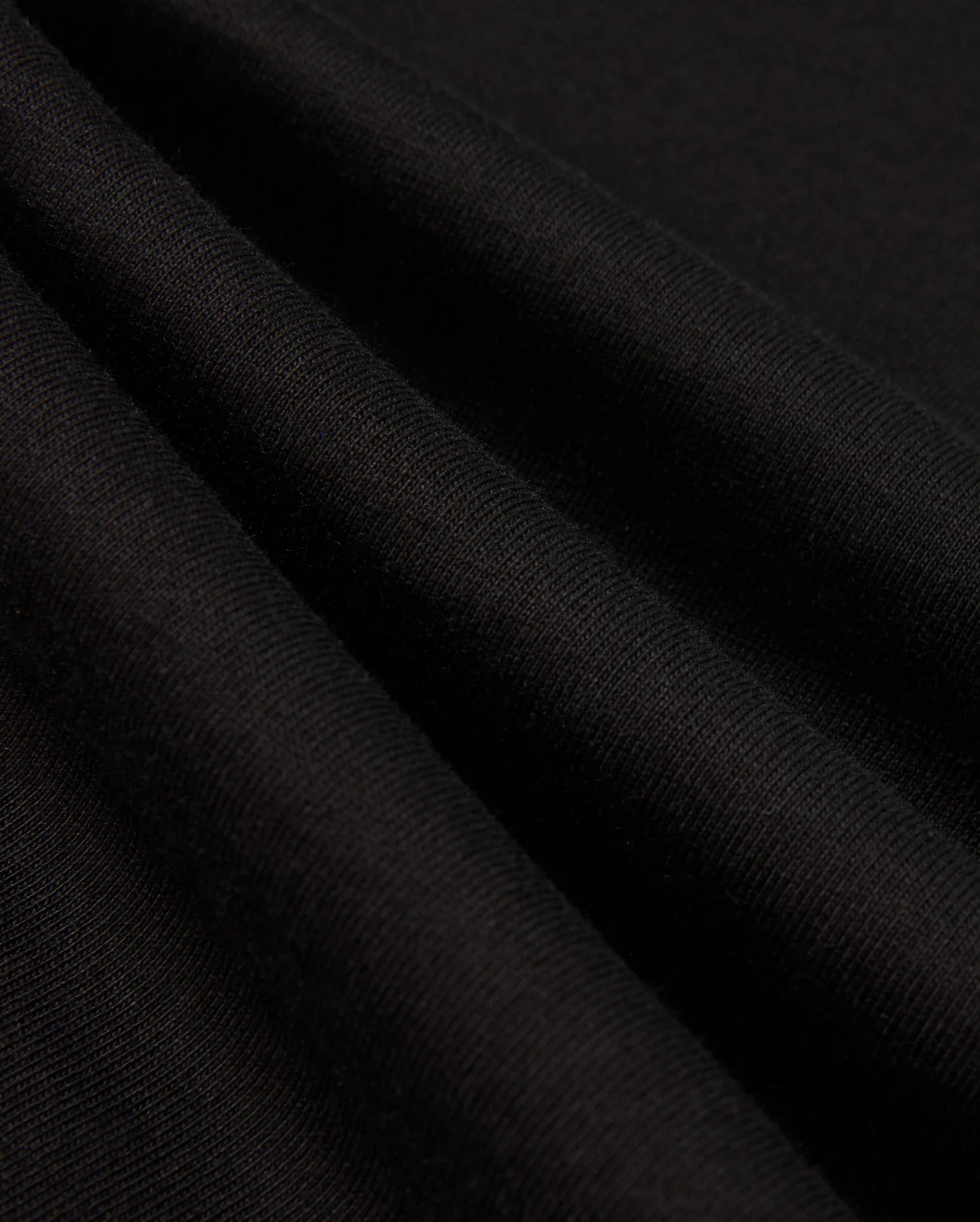 Close-up of the black Pima cotton fabric folds from the Psycho Bunny MENS ALBERTON LONG SLEEVE TEE - B6T867D200, showcasing a smooth, soft texture and fine weave. The wrinkles create subtle shadows, highlighting the material's flexibility and quality—truly a fashion masterpiece.