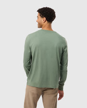 A person with short curly hair is wearing the Psycho Bunny MENS ALBERTON LONG SLEEVE TEE in light green, made from Pima cotton, along with beige pants. They are standing and facing away from the camera against a plain background.