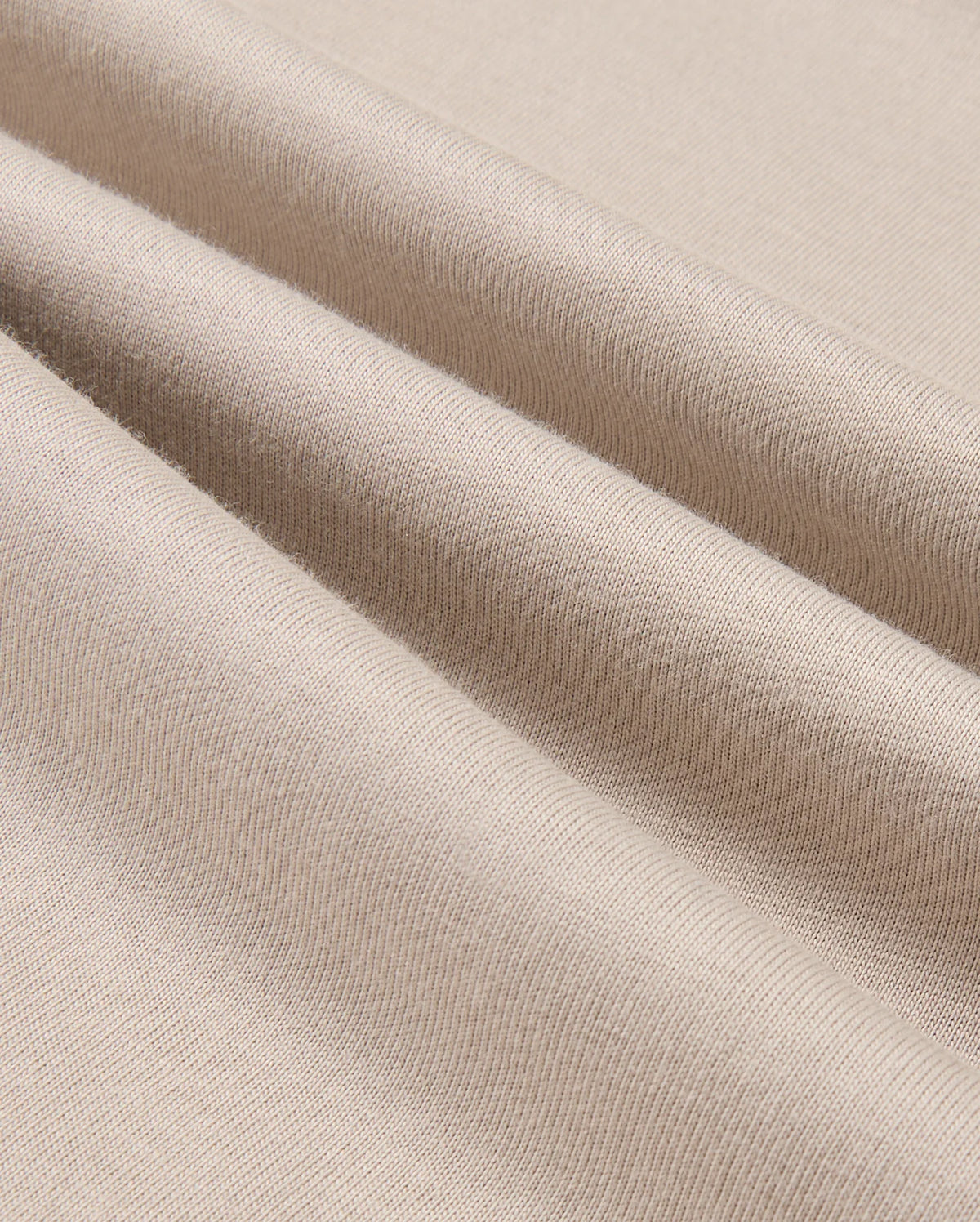 A close-up of the MENS ALBERTON LONG SLEEVE TEE - B6T867D200 by Psycho Bunny highlights the beige fabric elegantly folded to showcase its smooth texture and fine weave. This Pima cotton tee exemplifies flexibility and softness, making it the perfect choice for a luxurious layering piece.