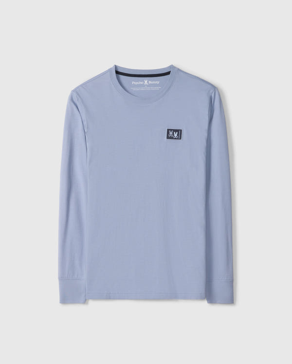 The Psycho Bunny MENS MONROE LONG SLEEVE TEE - B6T975D200, in light blue, is a comfortable long-sleeve t-shirt made from pima cotton. It features a round neckline and a small black patch with a white design on the upper chest for added versatile style.