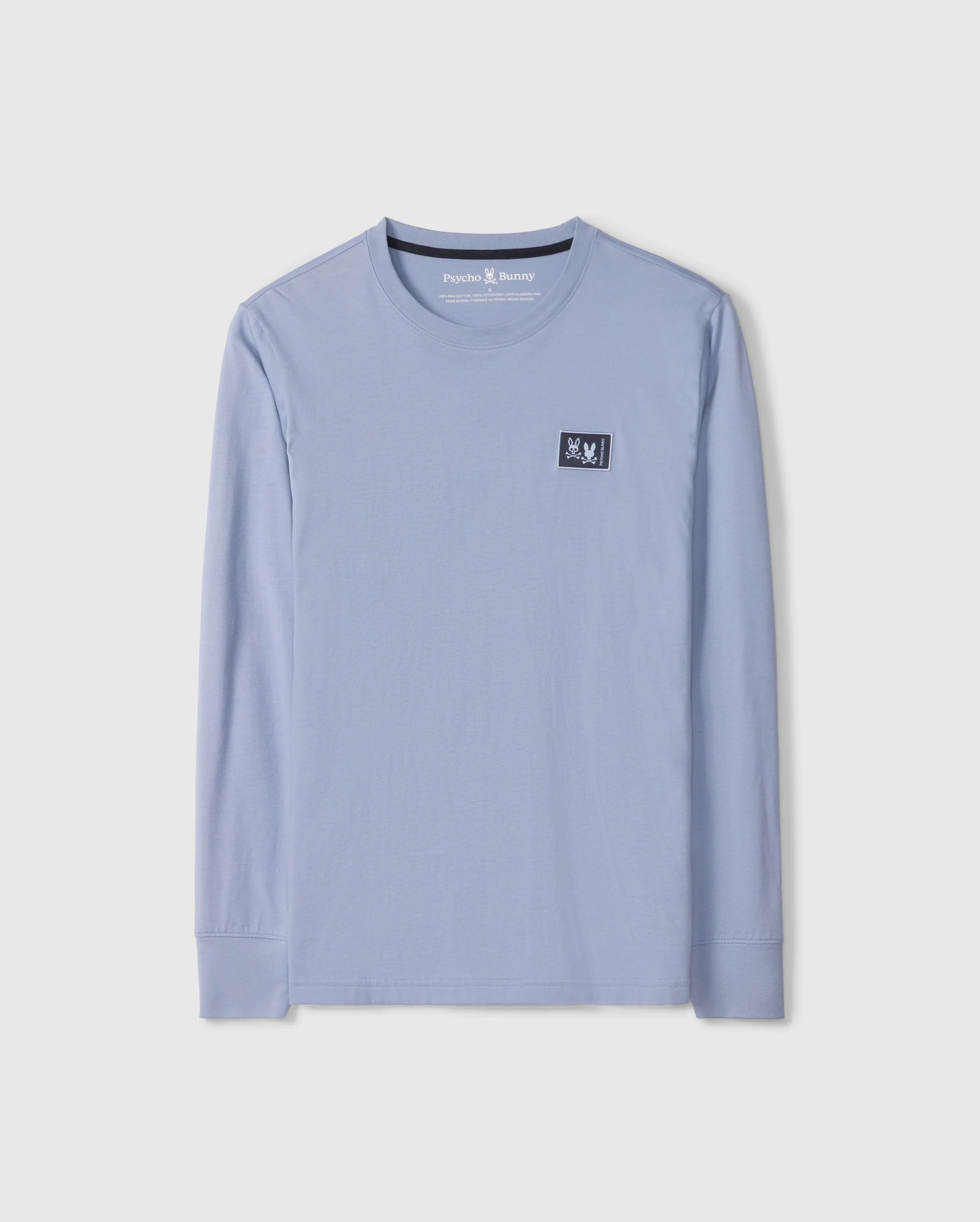 The Psycho Bunny MENS MONROE LONG SLEEVE TEE - B6T975D200, in light blue, is a comfortable long-sleeve t-shirt made from pima cotton. It features a round neckline and a small black patch with a white design on the upper chest for added versatile style.