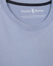 Close-up of a light blue Psycho Bunny Men's Monroe Long Sleeve Tee, highlighting its versatile style. The neckline and upper chest are visible, featuring a label inside the collar that reads "100% Pima Cotton" and "Made in Peru," promising classic comfort and quality.