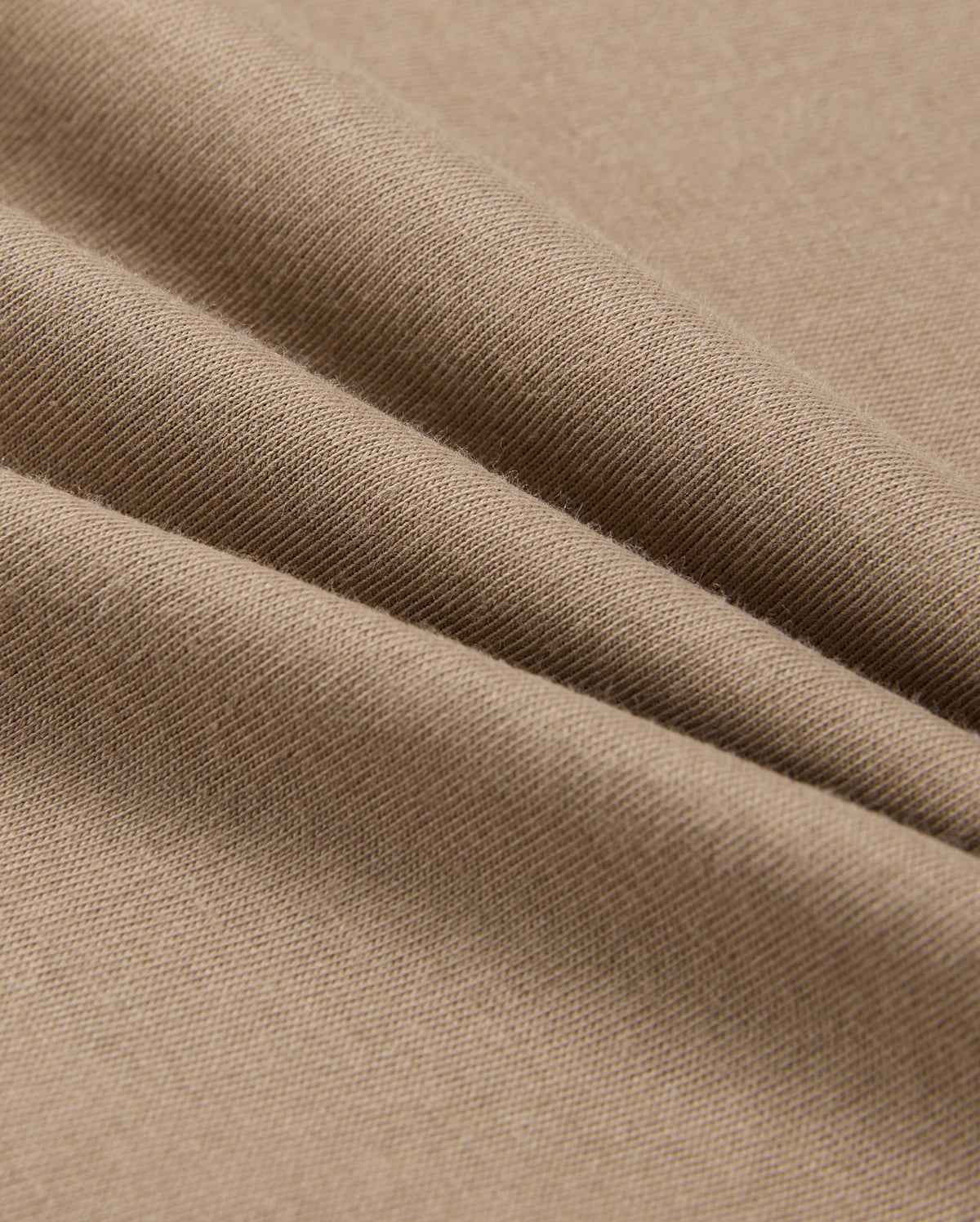 Close-up of a light brown fabric, showcasing soft folds and a smooth texture. Crafted from 100% Pima cotton, this material is stretchy and comfortable, making it perfect for the Psycho Bunny Men's Classic Crew Neck Tee (B6U014CRPC).