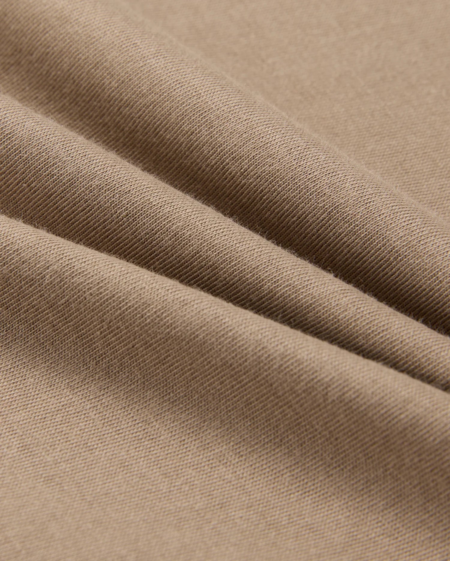 Close-up of a light brown fabric, showcasing soft folds and a smooth texture. Crafted from 100% Pima cotton, this material is stretchy and comfortable, making it perfect for the Psycho Bunny Men's Classic Crew Neck Tee (B6U014CRPC).