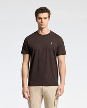 A person with short, curly hair wears a Psycho Bunny MENS CLASSIC CREW NECK TEE - B6U014B200 made of soft Pima cotton jersey and light-colored pants, standing against a neutral background.