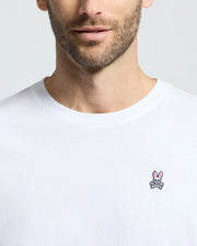 A man wearing a Psycho Bunny men's classic crew neck tee, B6U014CRPC, made of 100% Pima cotton with a small pink bunny and crossbones logo on the chest.