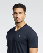 A person with short curly hair and a goatee is wearing the MENS CLASSIC V NECK TEE - B6U100ARPC, a Pima cotton V-neck T-shirt by Psycho Bunny, featuring an embroidered bunny logo in classic navy. The background is plain white.