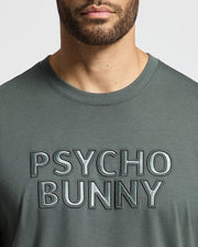 A person wearing a MENS PIERCE EMBROIDERED GRAPHIC TEE by Psycho Bunny featuring an eye-catching green color and a striking "Psycho Bunny" graphic boldly embroidered across the chest. The vibrant hue of this tee stands out against the white background.