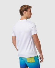 A man seen from behind, wearing a plain white Psycho Bunny MENS MAYBROOK GRAPHIC TEE - B6U130B2TS and colorful swim shorts, standing against a light background.
