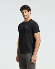 A person with curly hair stands confidently in a luxurious Psycho Bunny Men's Alexander Fashion Tee - B6U139E200 and dark pants against a light background.
