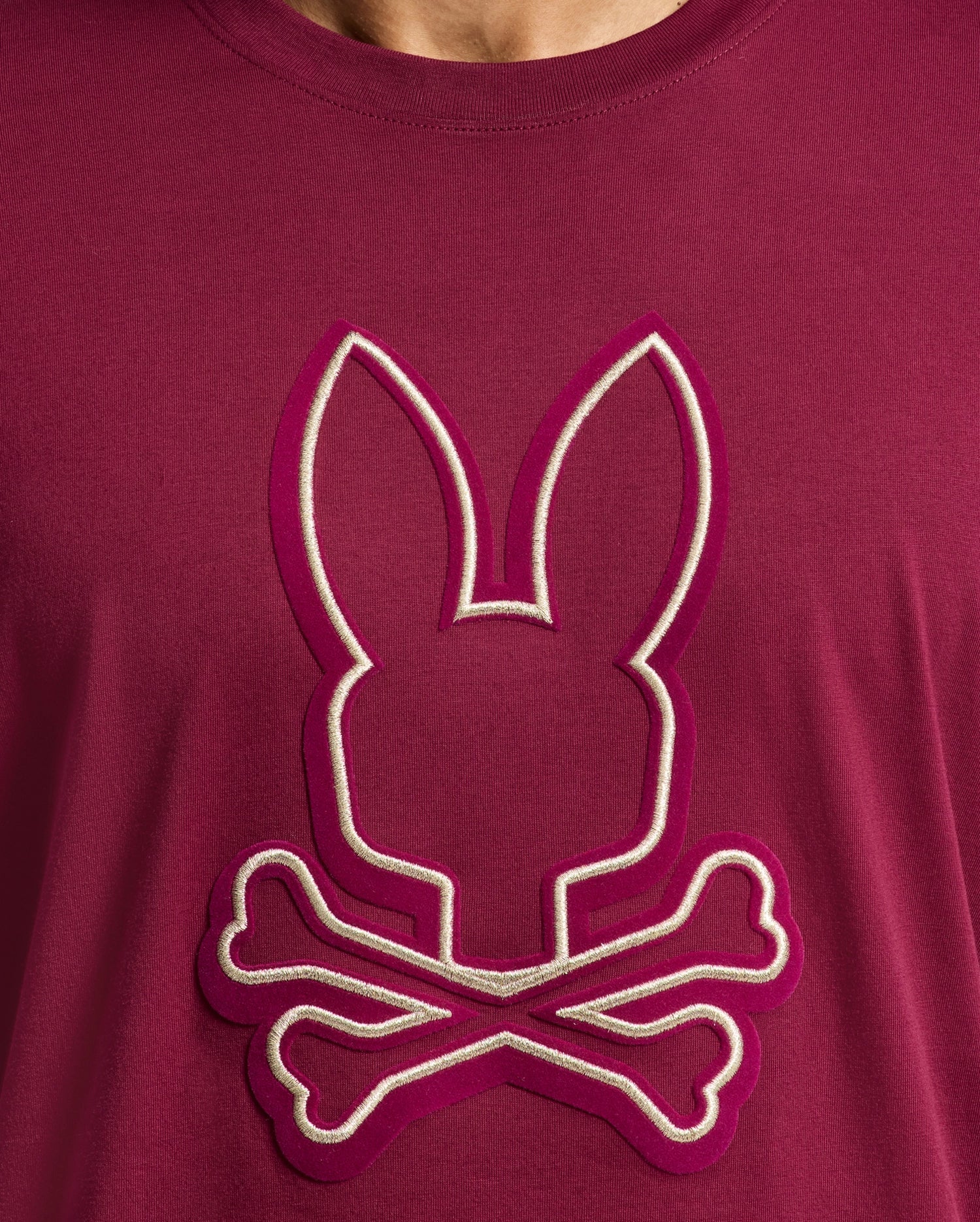 This maroon men's Alexander Graphic Tee by Psycho Bunny showcases a bold embroidered design of a stylized bunny head above crossed bones, accented in pink and white. Made from soft Pima cotton, it includes subtle Lurex details for a hint of sparkle.
