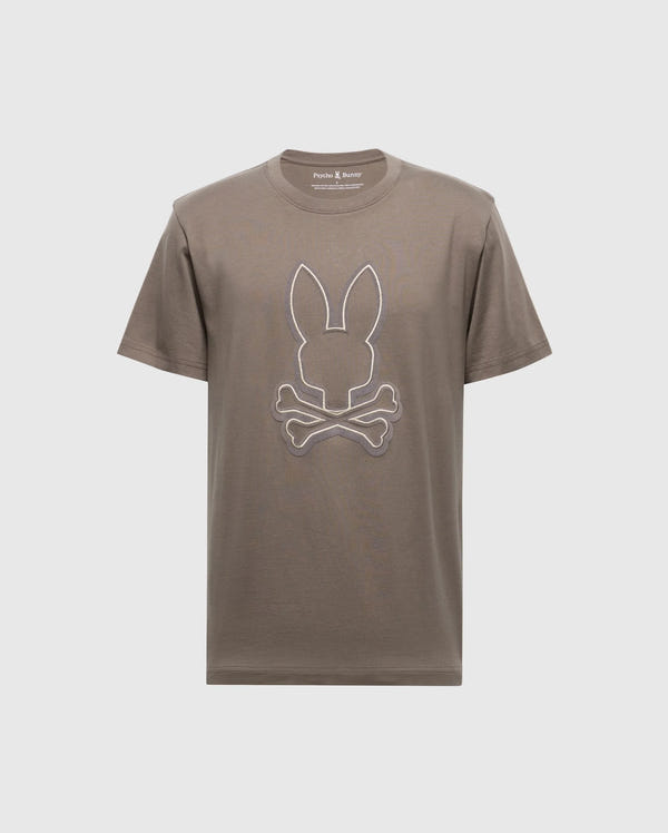 The Men's Alexander Graphic Tee - B6U163E200 by Psycho Bunny features a bold brown color with a distinctive white outline of rabbit ears above crossed bones, reminiscent of the classic skull and crossbones motif. Crafted from soft Pima cotton, it ensures both comfort and style in one unique package.