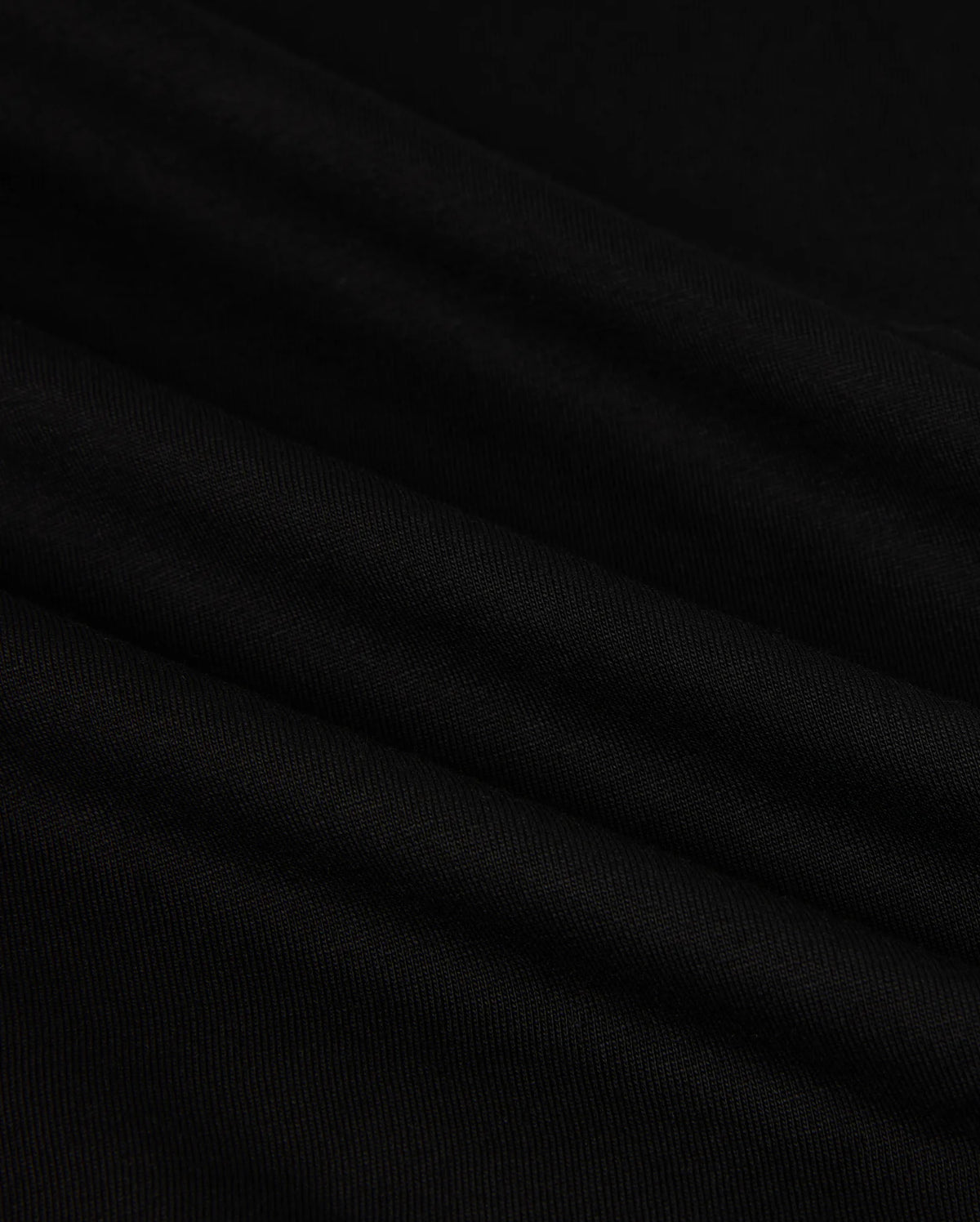 Close-up of the MENS HAWAII CITY TEE - B6U169Y1PC by Psycho Bunny, made from black Pima cotton fabric with a smooth, slightly rippled texture. The dark material displays gentle folds and a subtle sheen, resembling the luxurious quality of a sophisticated men's T-shirt for an elegant appearance.