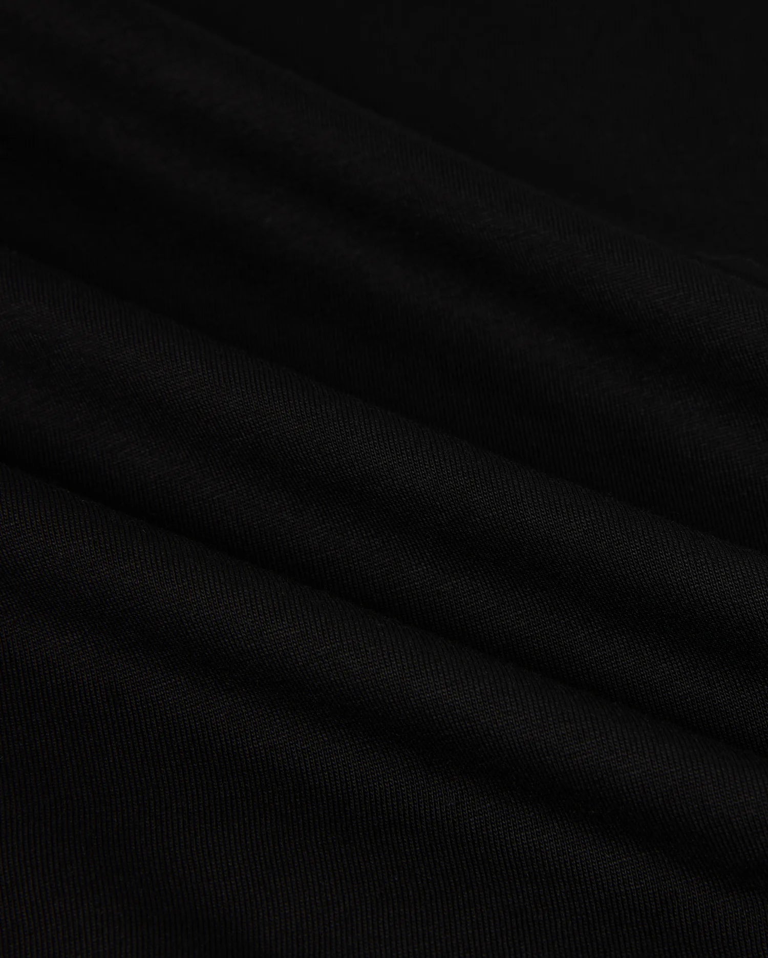 Close-up of the MENS HAWAII CITY TEE - B6U169Y1PC by Psycho Bunny, made from black Pima cotton fabric with a smooth, slightly rippled texture. The dark material displays gentle folds and a subtle sheen, resembling the luxurious quality of a sophisticated men's T-shirt for an elegant appearance.