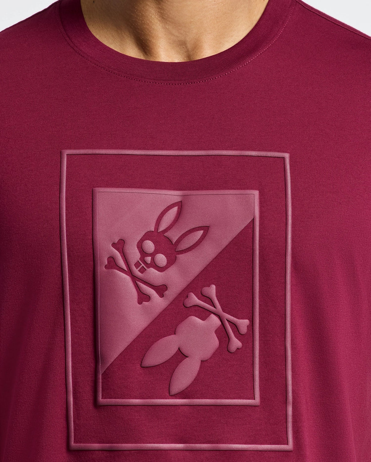 Close-up of the Psycho Bunny Men's Dotsero Graphic Tee - B6U197E200 in maroon, featuring a stylish textured skull and crossbones design with rabbit ears in a diagonal split square on the chest.