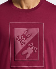 Close-up of the Psycho Bunny Men's Dotsero Graphic Tee - B6U197E200 in maroon, featuring a stylish textured skull and crossbones design with rabbit ears in a diagonal split square on the chest.