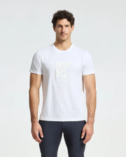 A man wearing a Psycho Bunny MENS DOTSER GRAPHIC TEE - B6U197E200, crafted from Pima cotton featuring a subtle embossed design on the front, pairs it with dark pants as he stands against a light gray background with his hands at his sides.
