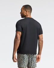 A person in a Psycho Bunny Mens Payson Leather Print Graphic Tee (B6U213E200) and patterned shorts stands sideways against a light background.