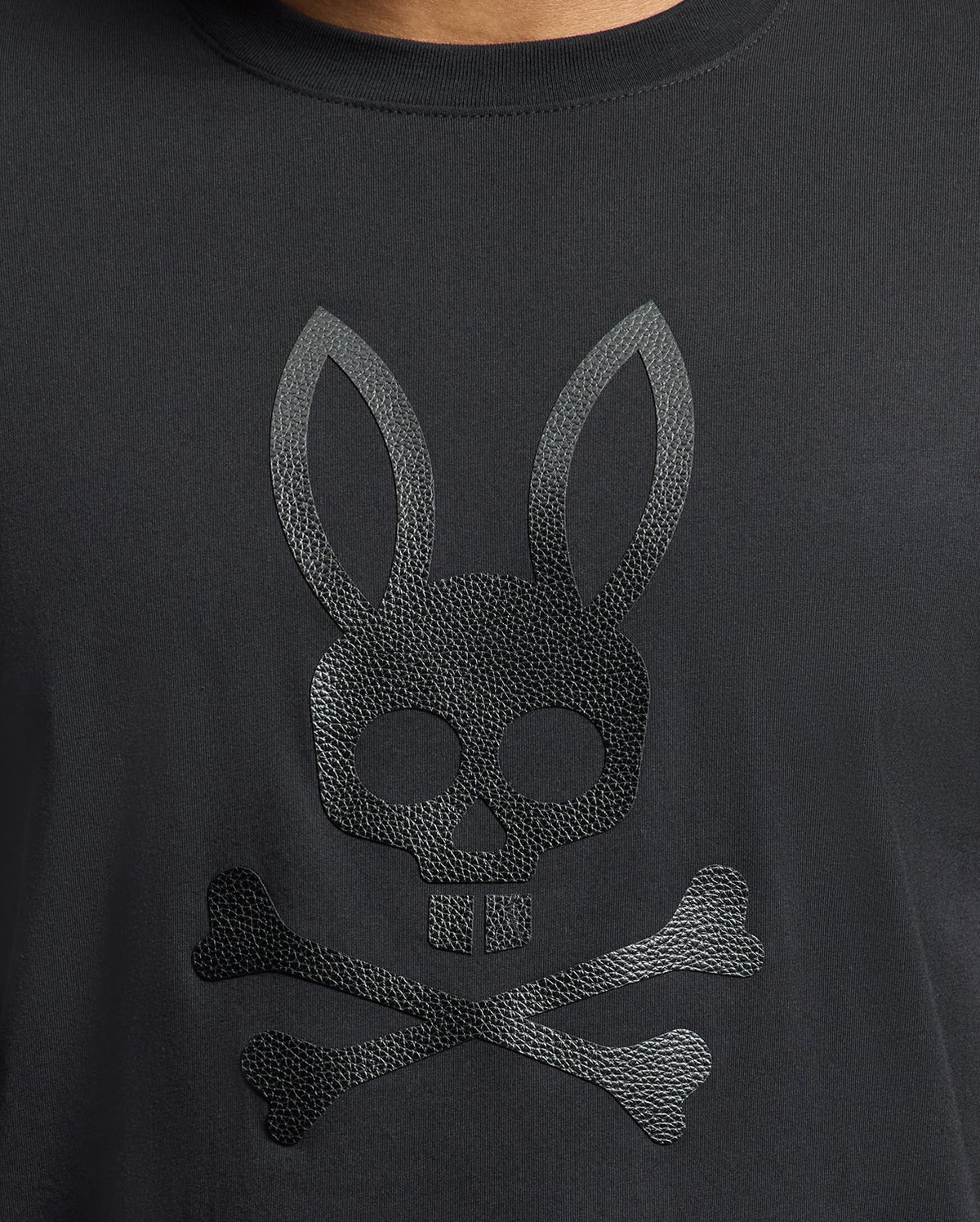 The Psycho Bunny MENS PAYSON LEATHER PRINT GRAPHIC TEE (B6U213E200) features a striking skull with rabbit ears above crossed bones design on soft Pima cotton jersey.