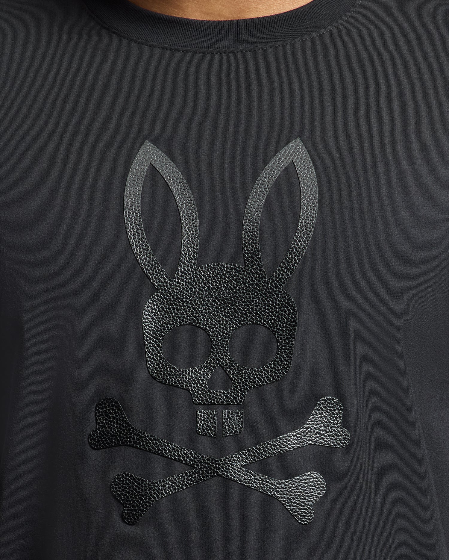 The Psycho Bunny MENS PAYSON LEATHER PRINT GRAPHIC TEE (B6U213E200) features a striking skull with rabbit ears above crossed bones design on soft Pima cotton jersey.