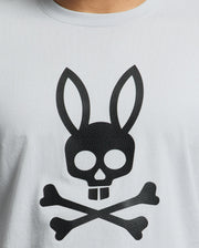 The Psycho Bunny MENS PAYSON LEATHER PRINT GRAPHIC TEE features a distinctive black skull with bunny ears and buck teeth, set above crossed bones on light gray Pima cotton. The leather print adds an edgy flair to this standout piece.