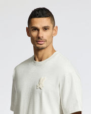 A man with short dark hair and a trimmed beard is wearing the Psycho Bunny MENS ELDORADO OVERSIZED TEE - B6U215E200, crafted from heavyweight Pima cotton jersey with an embroidered bunny and crossbones on the chest. The relaxed fit drapes comfortably as he stands against a plain background.