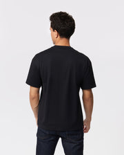 A person with short, dark hair is standing and facing away from the camera, wearing a plain black Psycho Bunny MENS OVERSIZED CLASSIC CREW NECK TEE - B6U240W1PC and dark blue jeans. The background is plain white.