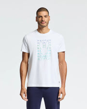 A man wearing Psycho Bunny's Men's Cortes Graphic Tee - B6U328E200, featuring a rabbit and geometric design on the front, pairs it with dark pants while standing against a plain background.