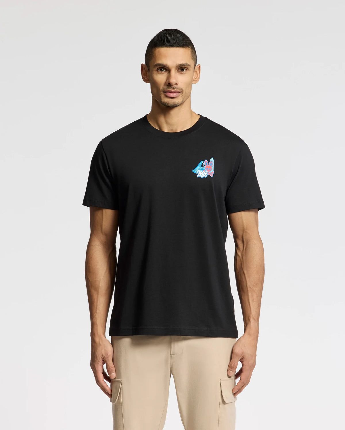 A man wearing a Psycho Bunny MENS TORONTO TEE - B6U383F200 made of Pima cotton, featuring a colorful mountain graphic on the left chest, pairs it perfectly with light tan pants against a white background.