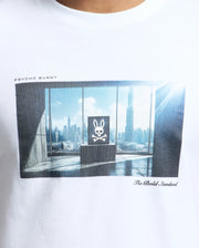 The MENS WARREN PHOTO REAL TEE - B6U388E200 by Psycho Bunny is a Pima cotton white T-shirt featuring a city skyline room print with a central skull and bunny ears. It displays "PSYCHO BUNNY" and "The Bold Standard.