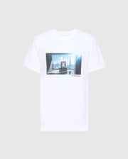 The MENS WARREN PHOTO REAL TEE - B6U388E200 by Psycho Bunny is a white Pima cotton jersey shirt showcasing a city skyline through large windows, with abstract elements and text graphics. Set against a gray background, this tee offers style and comfort for urban enthusiasts.