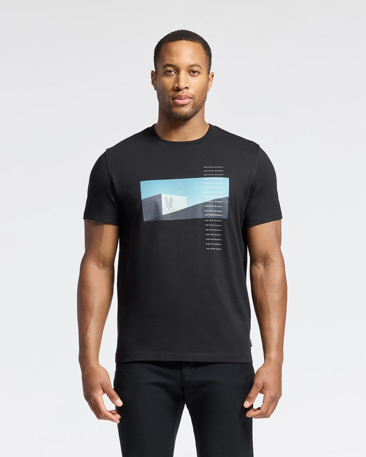 A man in the Psycho Bunny MENS NEIL PHOTO REAL TEE - B6U389E200, crafted from soft Pima cotton with a blue and white geometric gradient design, stands against a plain white background. His relaxed arms highlight the shirt's jersey fabric mirroring brutalist simplicity.